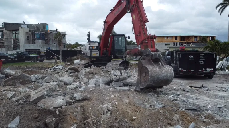 Red excavator on concrete rubble pile at waterfront demolition site on Longboat Key FL