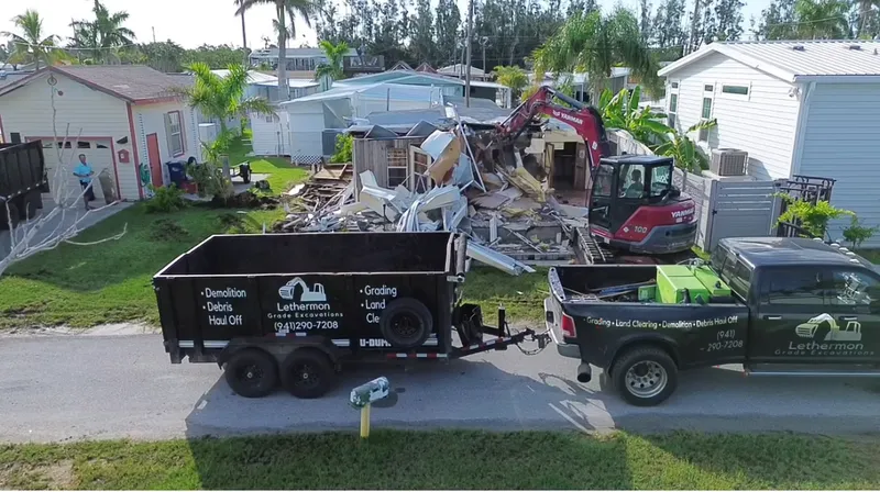 Red Yanmar excavator demolishing mobile home with branded Lethermon truck and trailer on site