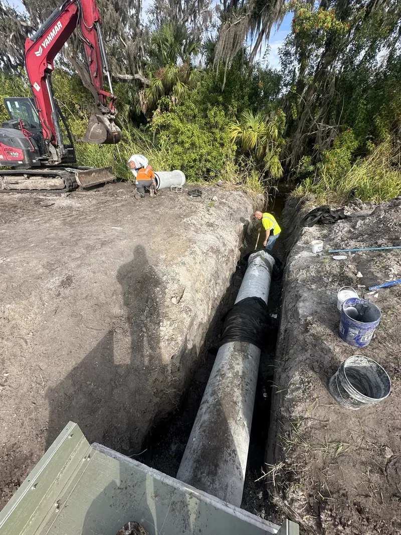 Crew working in deep trench installing large concrete culvert pipe with Yanmar excavator in Palmetto FL