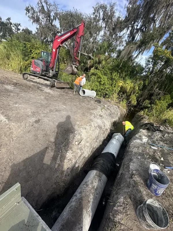 Yanmar excavator lifting large concrete pipe with crew during commercial drainage install in Palmetto FL
